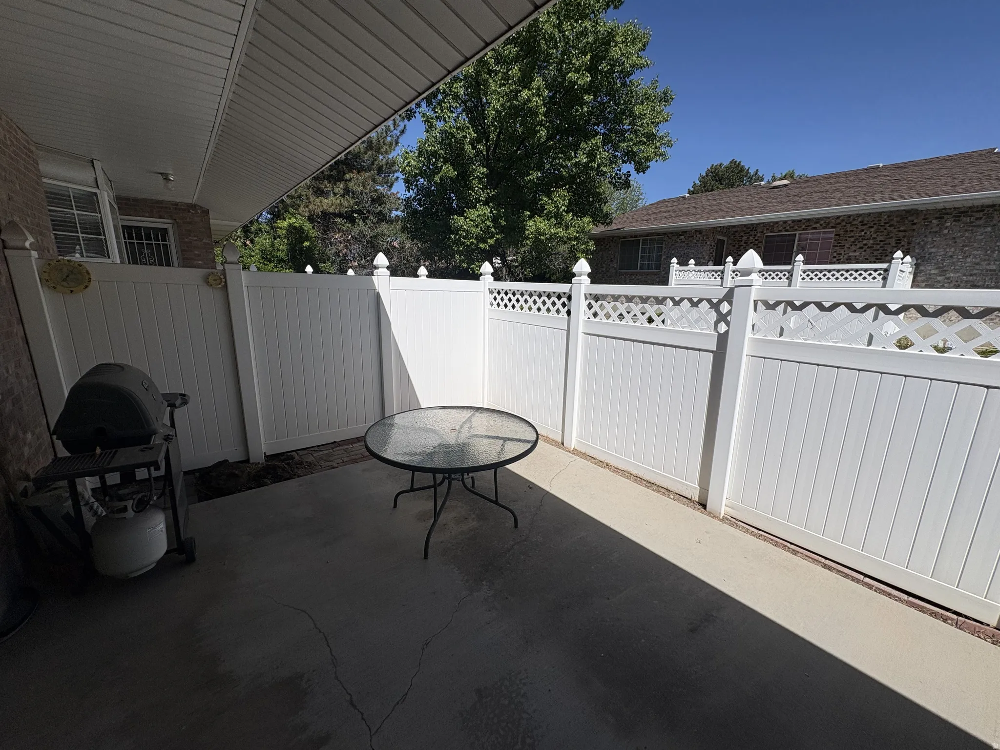 Private concrete patio featuring white vinyl fencing with decorative lattice accents and a covered overhang