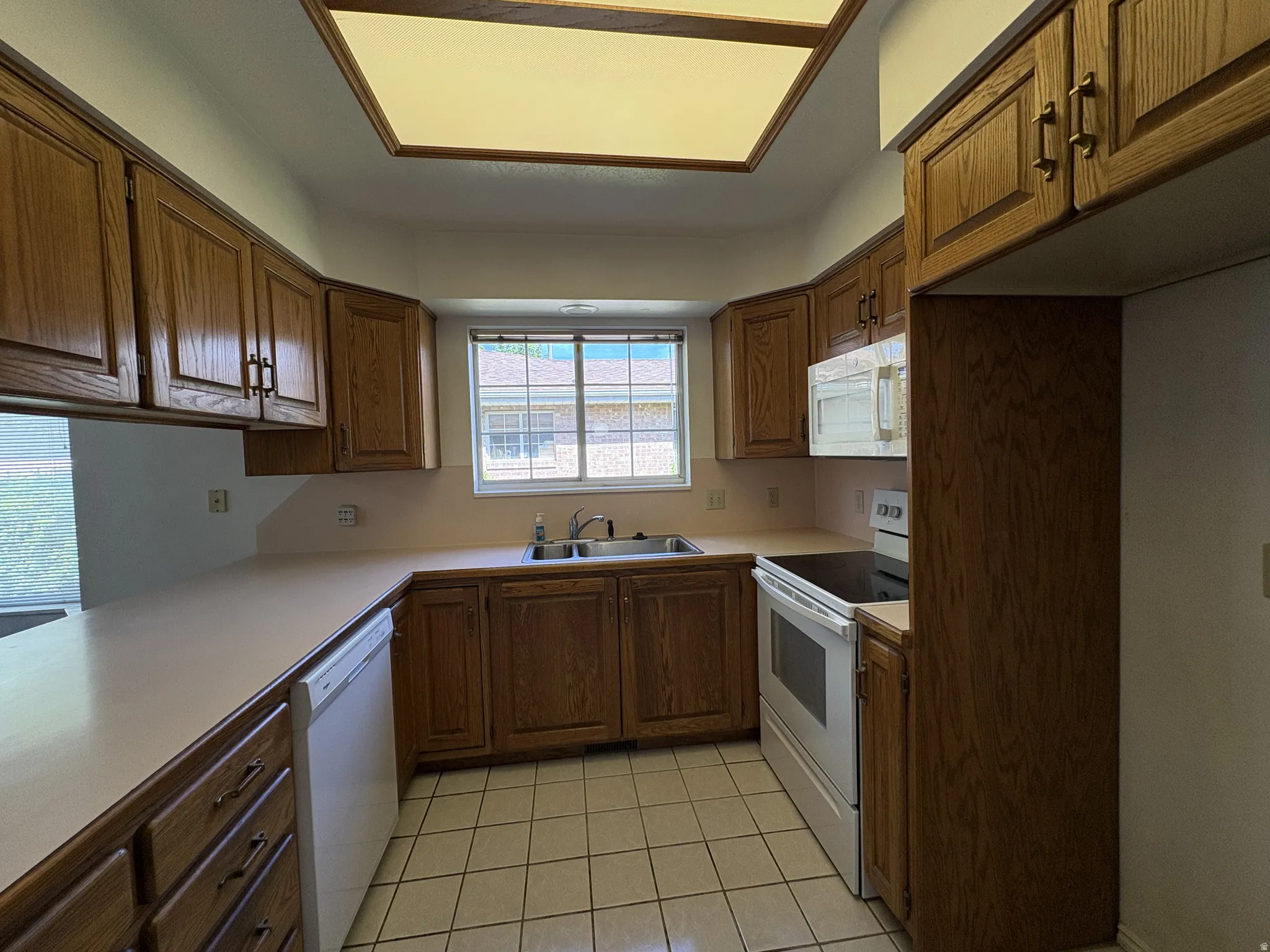 Kitchen featuring wood cabinetry, white appliances, laminate countertops, and a double basin sink