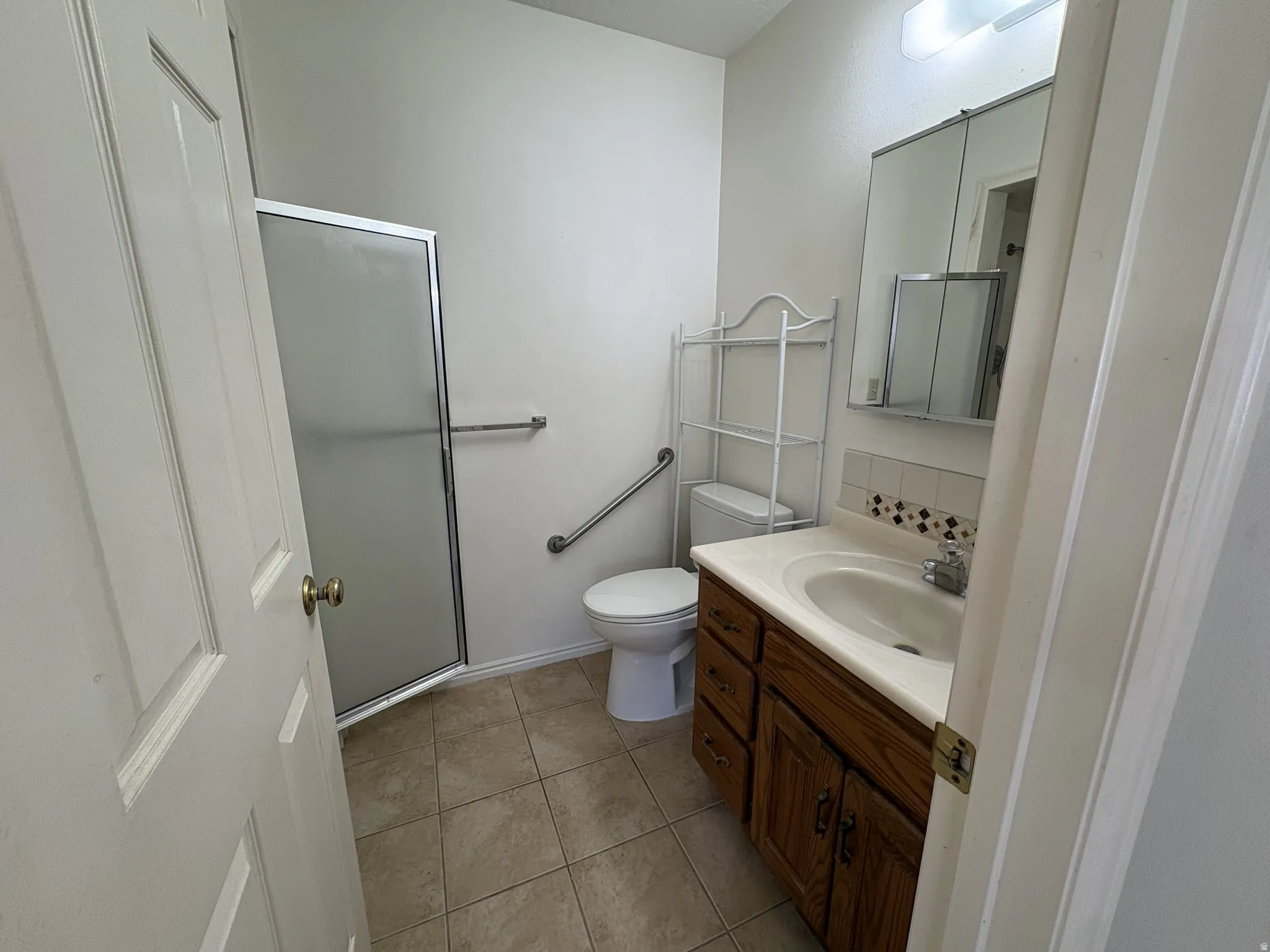 Bathroom featuring a glass-enclosed shower, a wood-finish vanity with an integrated sink, tile flooring, and a mirrored medicine cabinet
