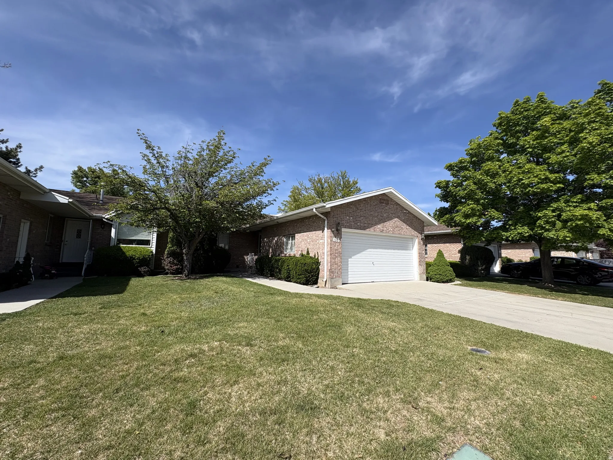 Brick exterior with an attached garage, concrete driveway, and mature landscaping