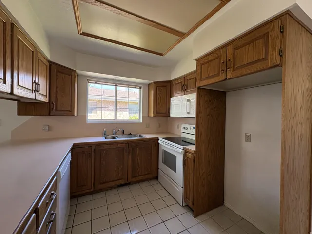 Kitchen with wood-finish cabinetry, solid surface countertops, and white tile flooring