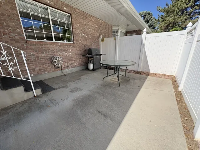 Private concrete patio area featuring a brick exterior wall and white vinyl fencing