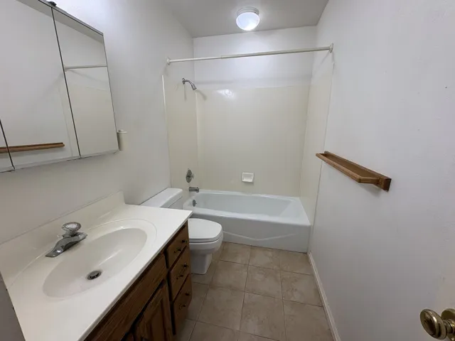 Bathroom featuring a wood-finish vanity with an integrated sink, a medicine cabinet with mirrored doors, a full-size bathtub with shower, and ceramic tile flooring