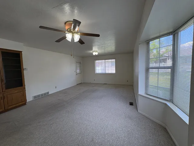 Spacious living area featuring light-toned carpeting and a ceiling fan with integrated lighting