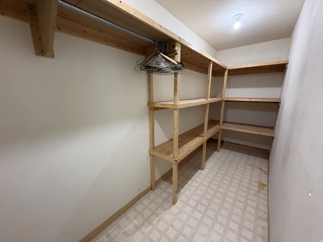 Storage room with patterned flooring, built-in wooden shelving, and a hanging rod