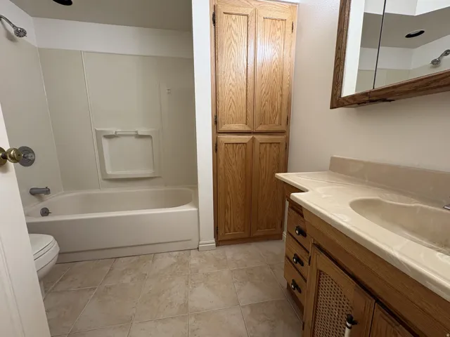 Full bathroom featuring a single vanity with integrated sink, wood-finish cabinetry, built-in shelving, a shower/tub combination, and tiled flooring