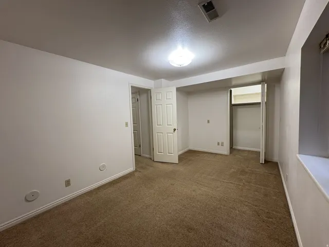 Carpeted room featuring white walls, white trim, a flush-mount ceiling light, a built-in closet with bifold doors, and a window well