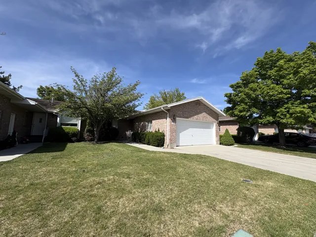 Brick exterior with an attached garage, concrete driveway, and mature landscaping