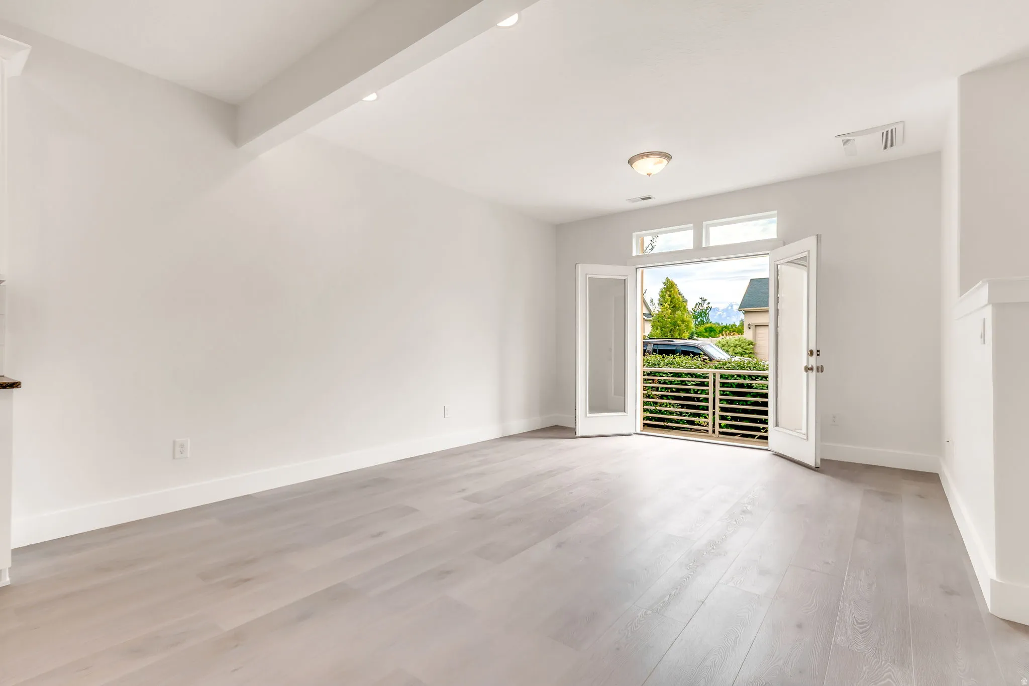 Spacious room featuring wood-finish flooring, white walls, and a recessed ceiling beam