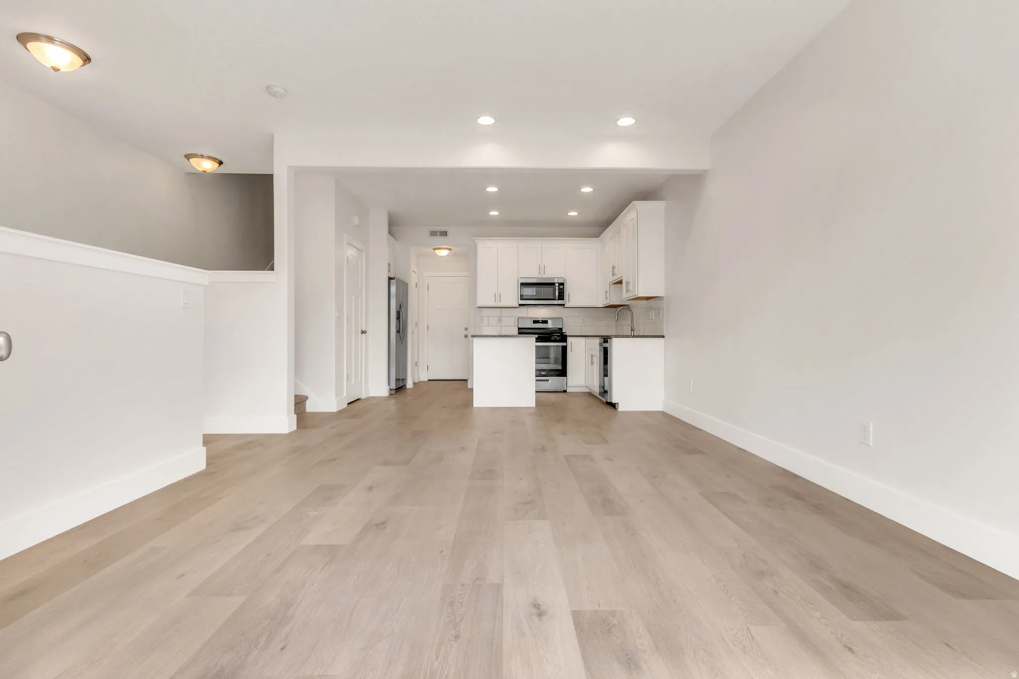 Open-concept living space featuring wood-finish flooring, recessed lighting, and a white kitchen with stainless steel appliances and subway tile backsplash
