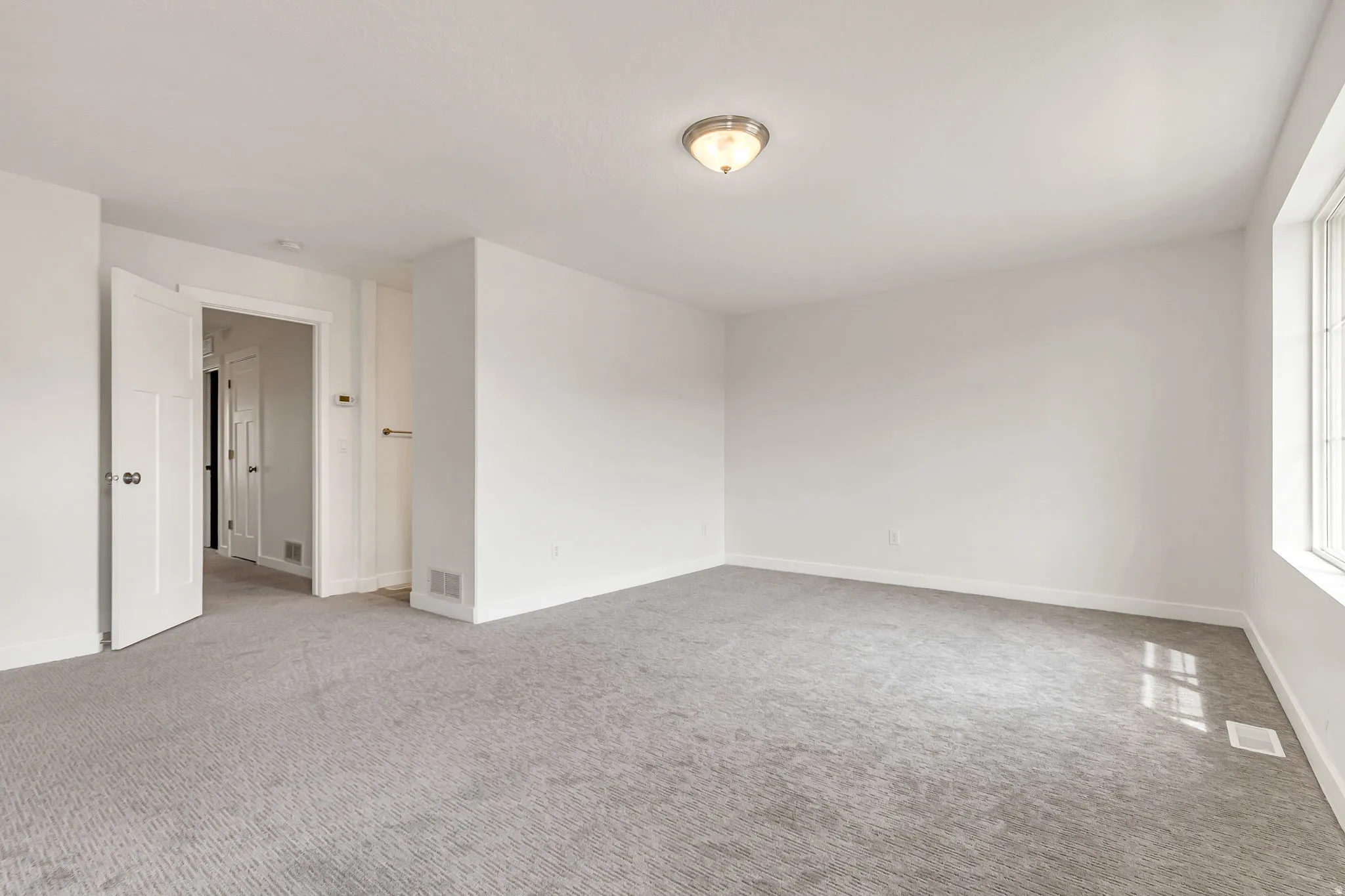 Spacious room featuring light gray carpet flooring, white painted walls, a large multi-pane window, and a flush-mount ceiling light fixture