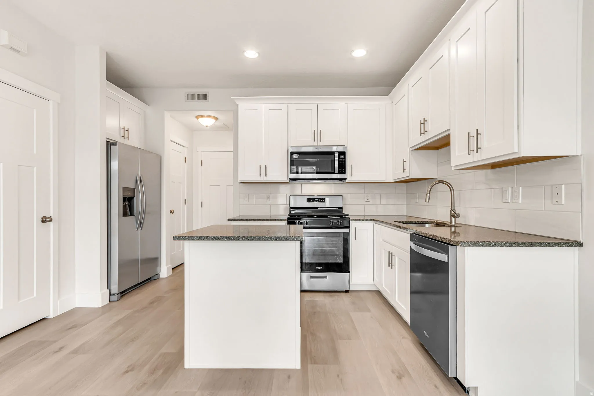 Modern kitchen featuring white shaker cabinetry, stainless steel appliances, speckled stone countertops, and wood-finish flooring