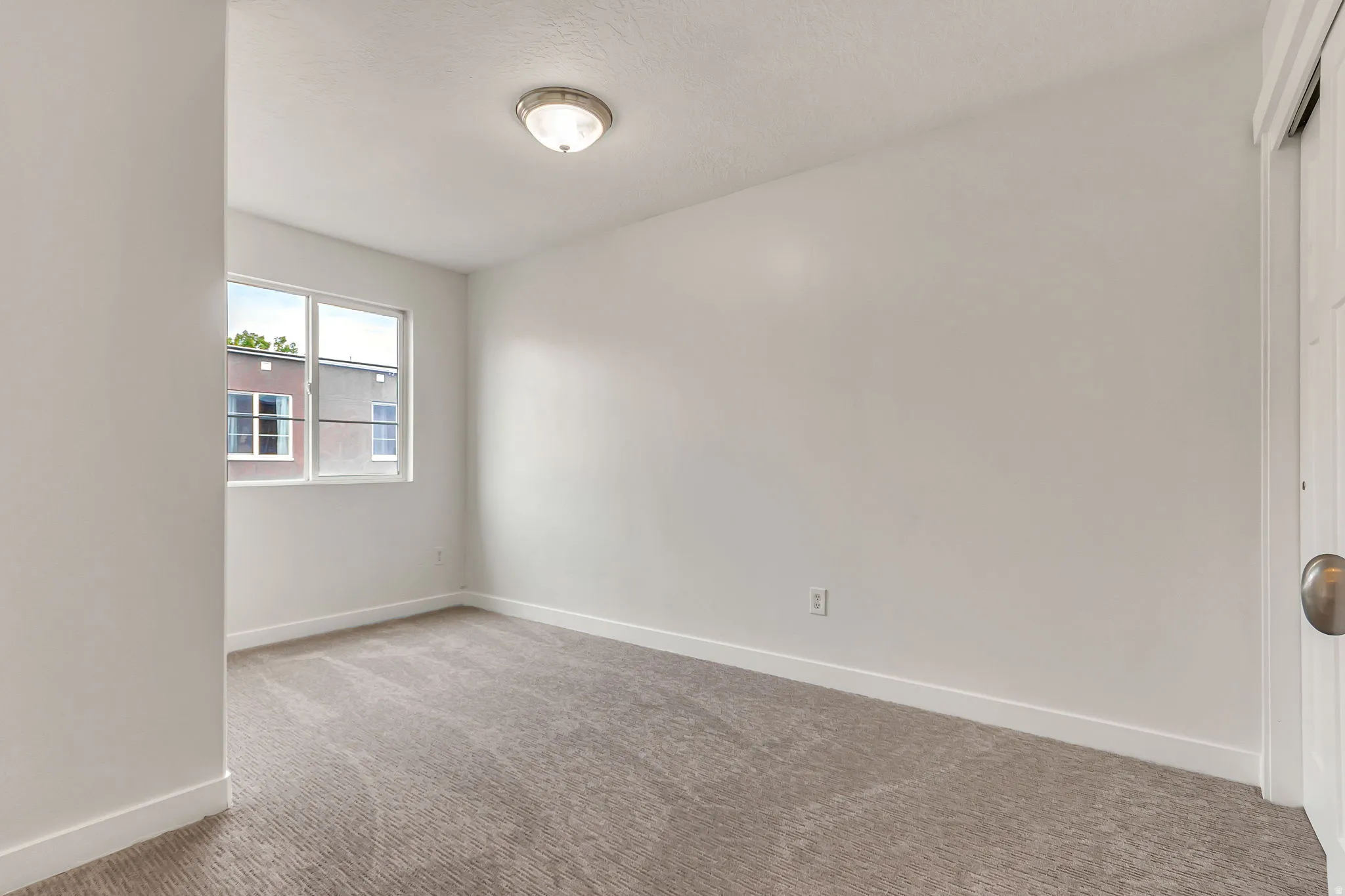 Bright interior space featuring a window, neutral carpet flooring, white baseboards, and a flush mount ceiling light