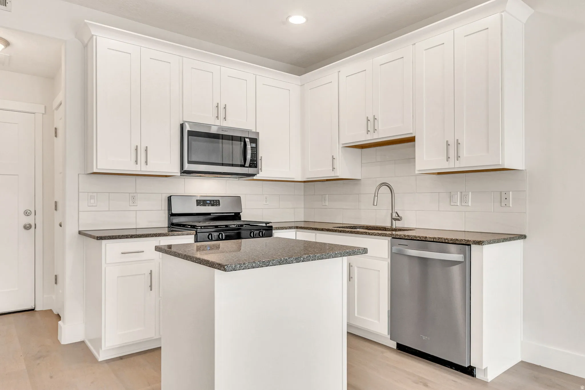 Modern kitchen featuring white shaker cabinetry, stainless steel appliances, speckled stone countertops, a white subway tile backsplash, and light wood-finish flooring