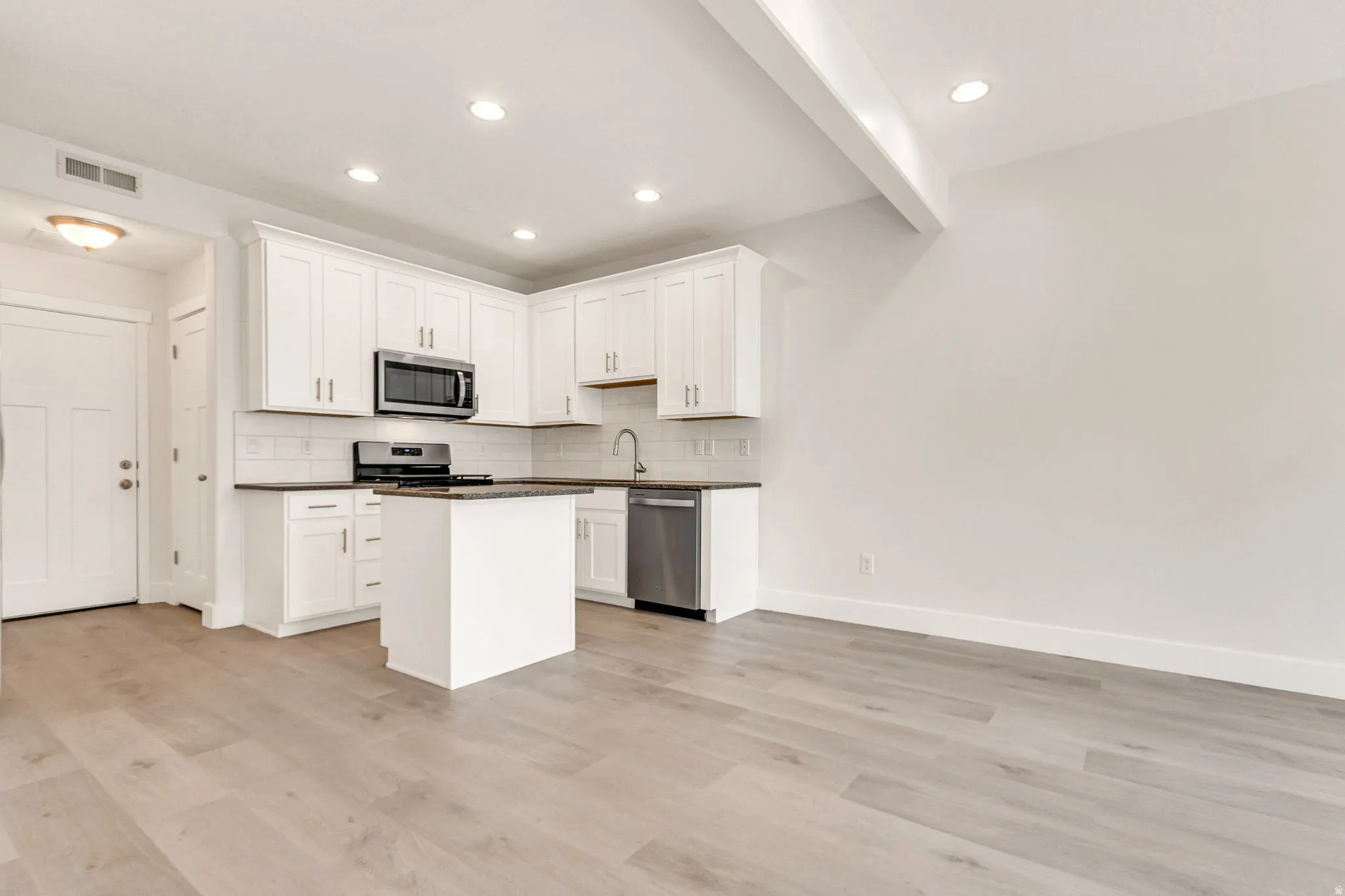 Open-concept kitchen and living area featuring light wood-finish flooring, white shaker cabinetry, stainless steel appliances, and a central island
