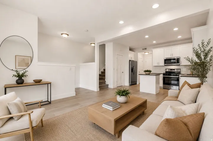 Open-concept living area featuring light wood-finish flooring, recessed lighting, white shaker cabinetry, stainless steel appliances, and a kitchen island with a dark countertop