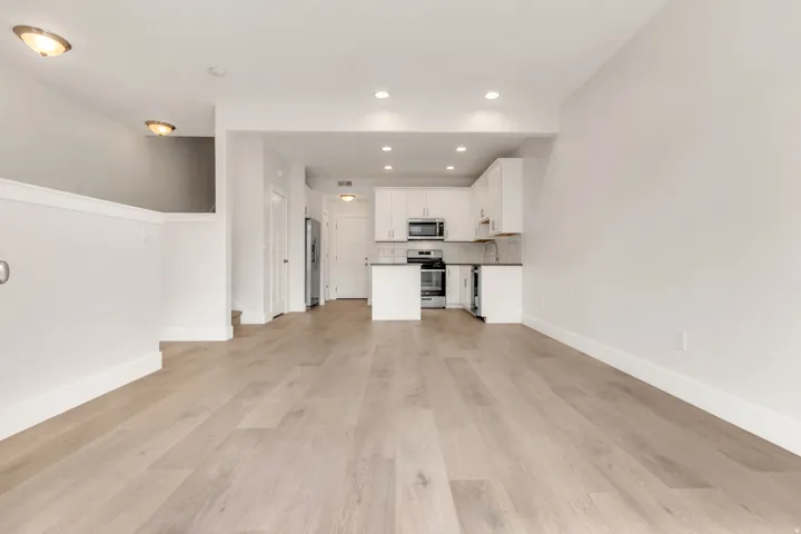 Open-concept living space featuring wood-finish flooring, recessed lighting, and a white kitchen with stainless steel appliances and subway tile backsplash