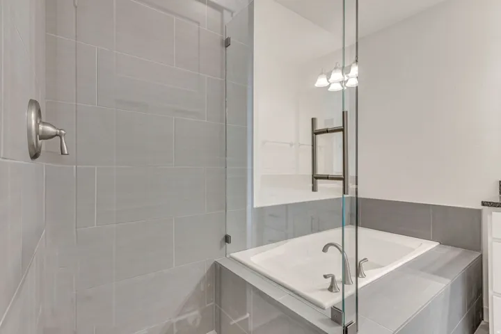 Glass-enclosed shower with light gray tile surround and brushed nickel fixtures