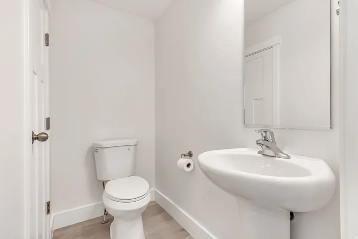 Pedestal sink with chrome faucet, toilet, and wood-finish flooring