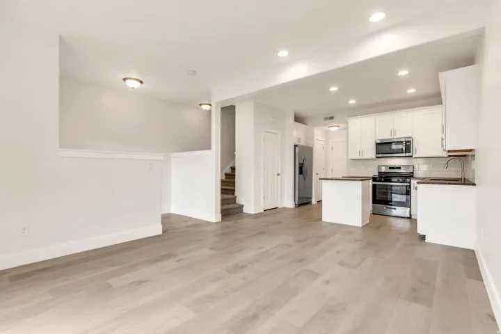 Open-concept living area featuring wood-finish flooring, recessed lighting, and a kitchen with white cabinetry, stainless steel appliances, and a tiled backsplash