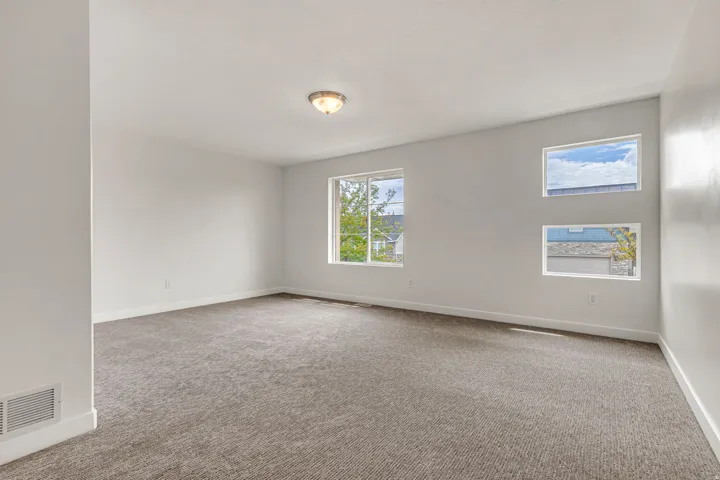 Spacious room featuring neutral carpeting, white painted walls, and multiple windows providing ambient light
