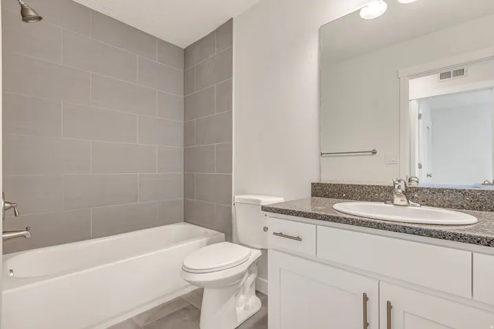 Bathroom featuring a white bathtub, gray subway tile surround, and a vanity with a dark speckled countertop