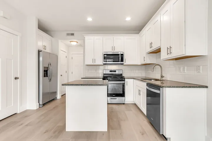 Modern kitchen featuring white shaker cabinetry, stainless steel appliances, speckled stone countertops, and wood-finish flooring