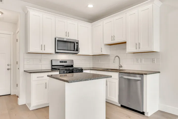 Modern kitchen featuring white shaker cabinetry, stainless steel appliances, speckled stone countertops, a white subway tile backsplash, and light wood-finish flooring