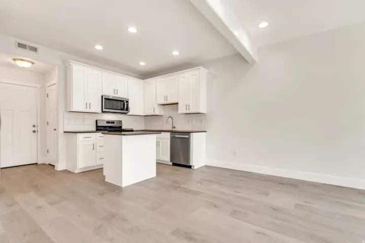 Open-concept kitchen and living area featuring light wood-finish flooring, white shaker cabinetry, stainless steel appliances, and a central island