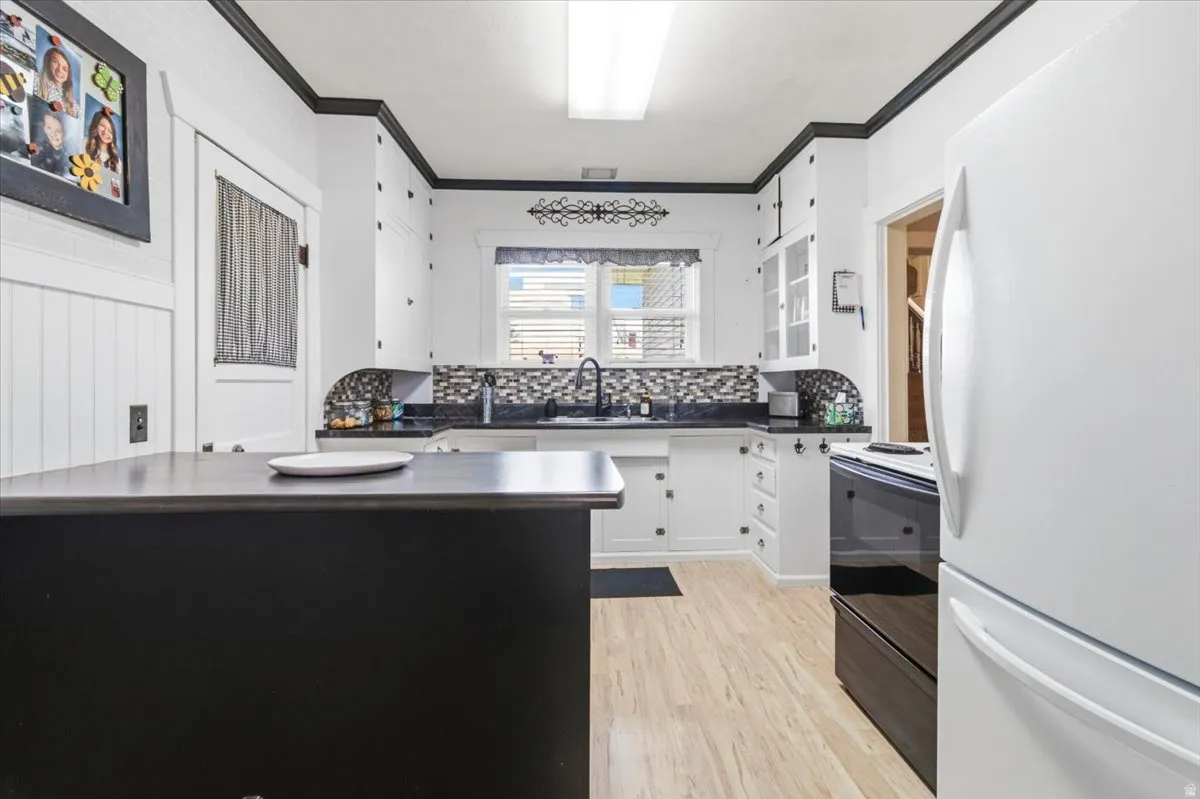 Kitchen featuring wood-finish flooring, white cabinetry with dark trim, dark countertops, and a mosaic tile backsplash