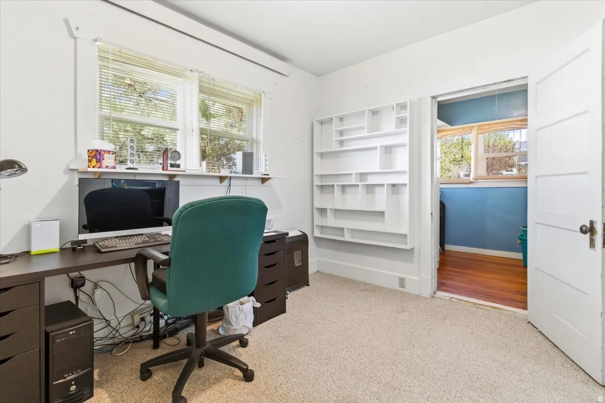 Carpeted room with a built-in shelving unit, dual windows with blinds, and a white paneled door