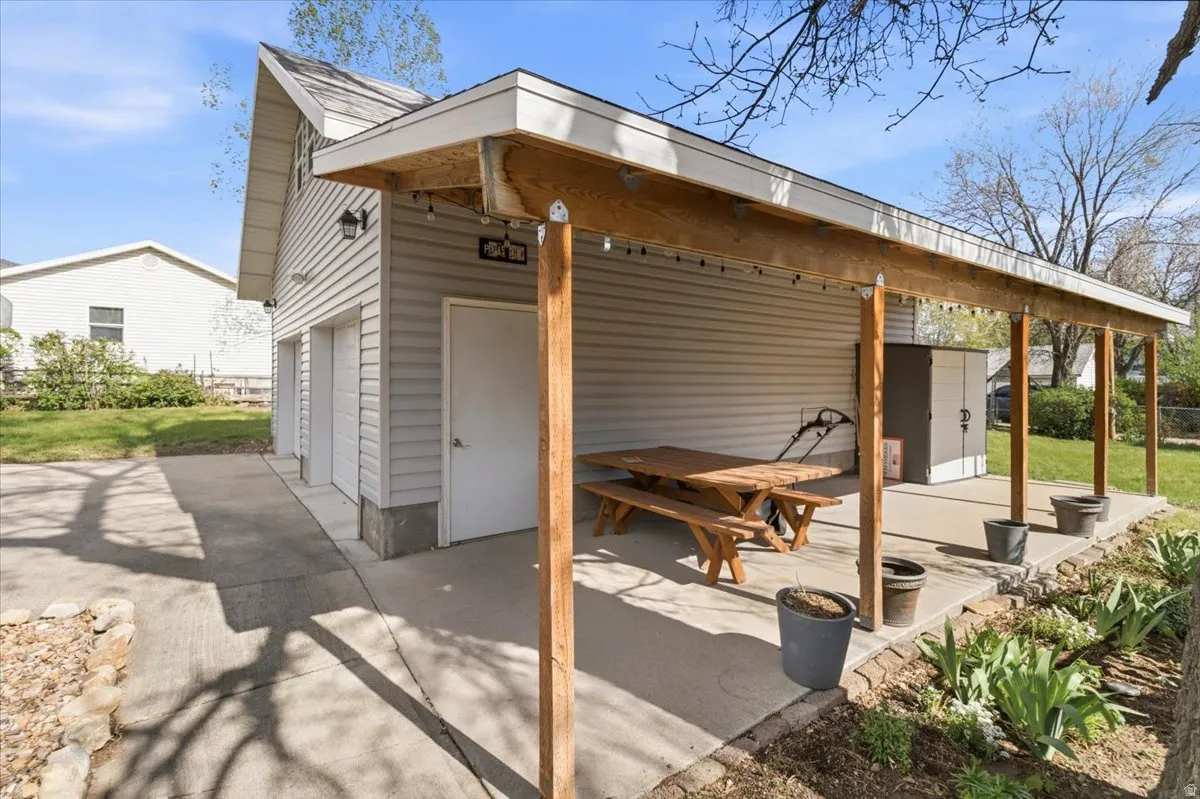 Covered patio area with wood support beams, string lighting, and a concrete pad