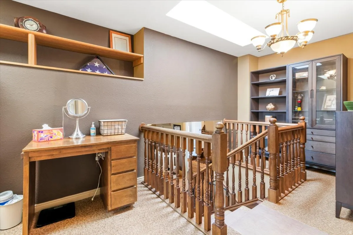 Upper-level landing featuring wood banister, built-in shelving, a skylight, and an overhead chandelier