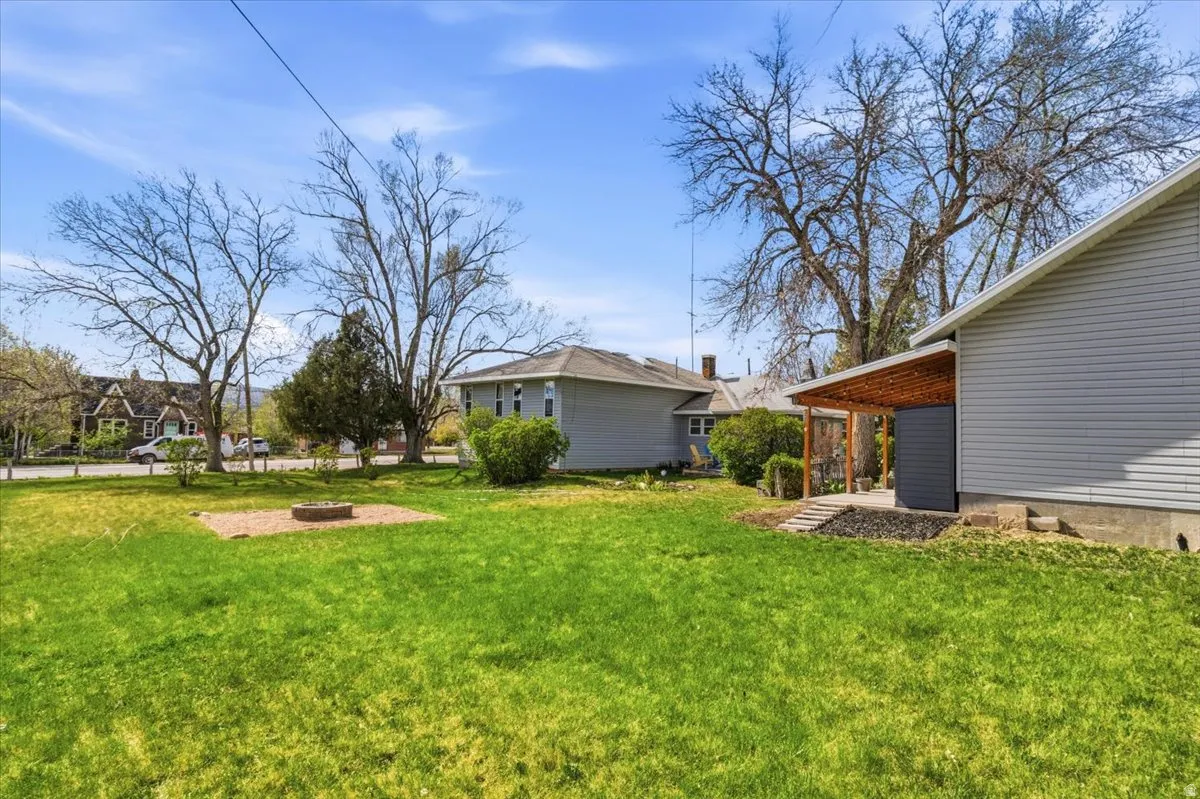 Expansive lawn with a fire pit area, mature trees, and a covered patio with a wood slat roof structure