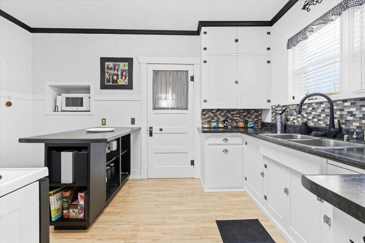 Kitchen featuring white cabinetry with dark hardware, dark countertops, and a mosaic tile backsplash
