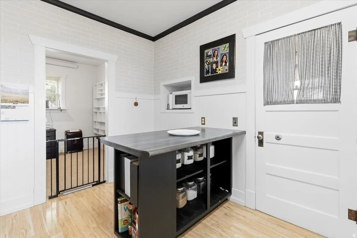 Kitchen area with wood-finish flooring, white brick-patterned walls, and contrasting dark trim