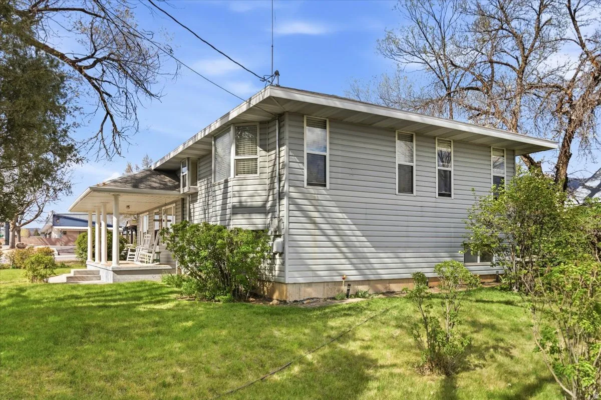 Light gray siding exterior with multiple windows, a covered front porch supported by white columns, and a grassy front yard