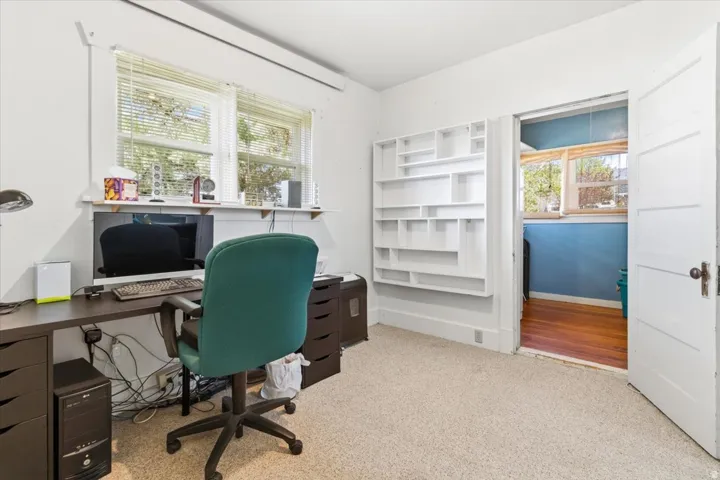 Carpeted room with a built-in shelving unit, dual windows with blinds, and a white paneled door