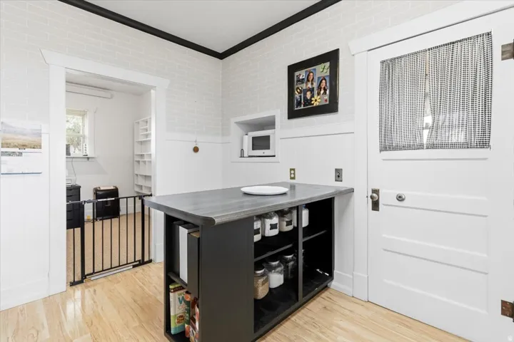 Kitchen area with wood-finish flooring, white brick-patterned walls, and contrasting dark trim