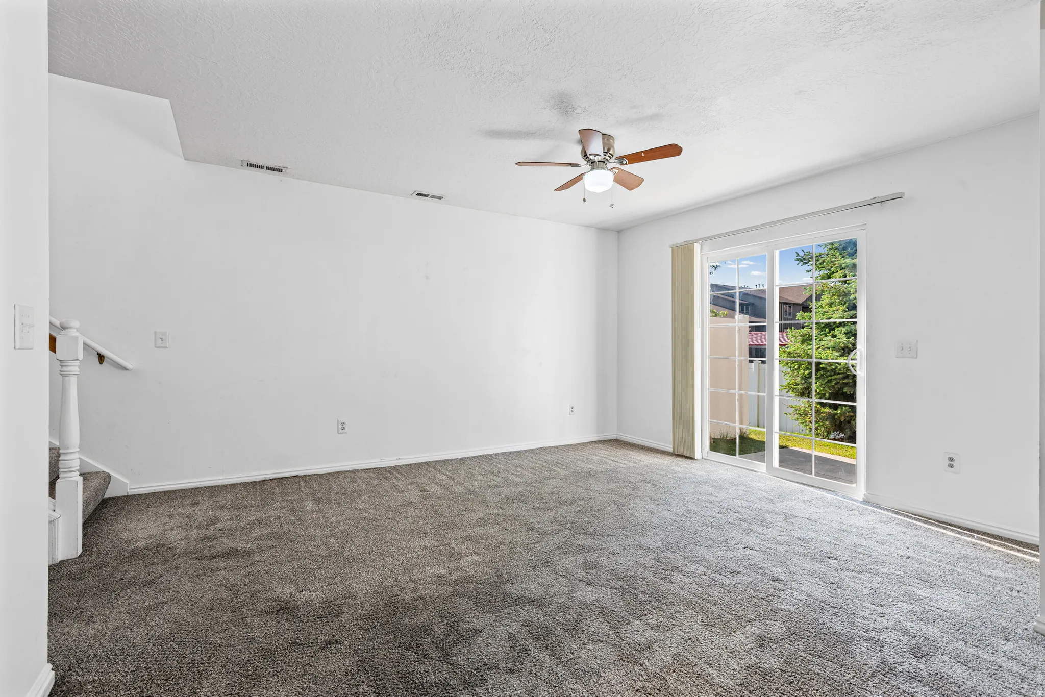 Carpeted living area featuring a ceiling fan with light, white wall finishes, and a sliding glass door
