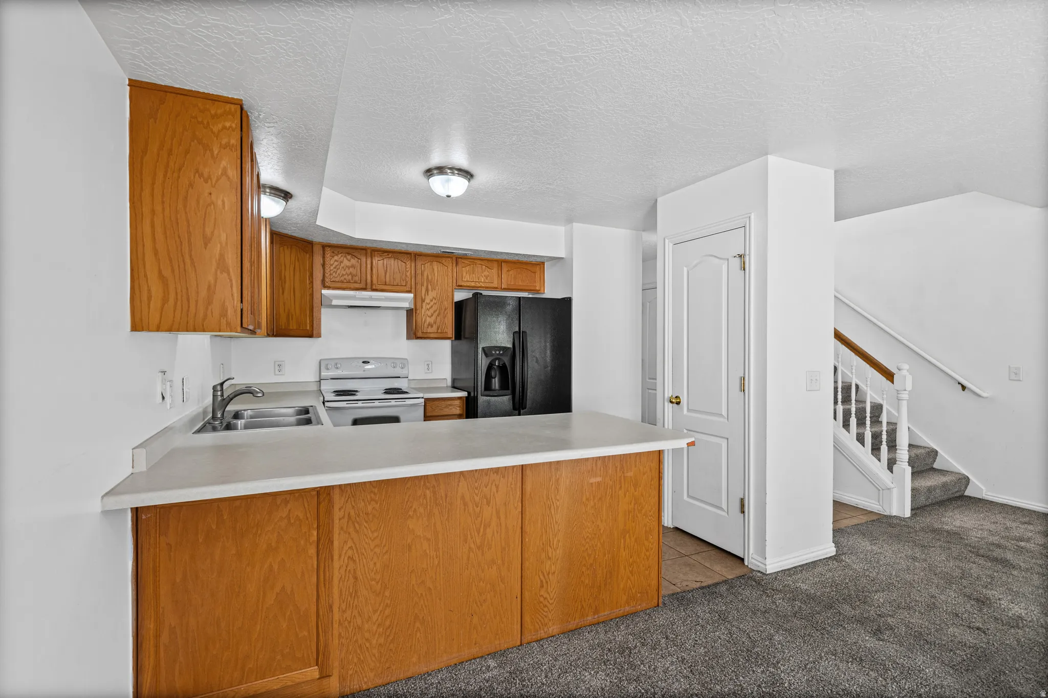 Kitchen featuring wood cabinetry, laminate countertops, a stainless steel double sink, and white appliances