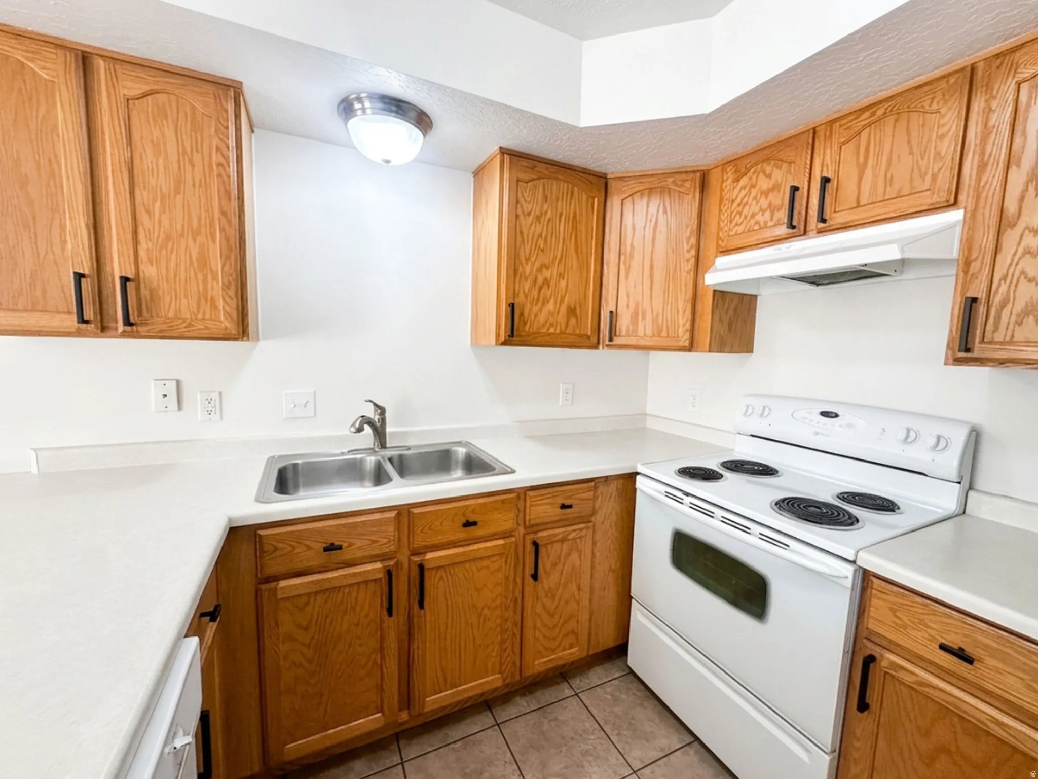 Kitchen featuring wood cabinetry, white countertops, a stainless steel double basin sink, and a white electric range with an overhead exhaust fan