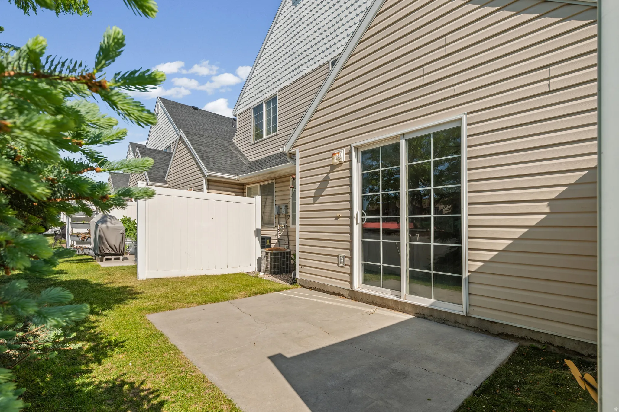 Rear exterior with a concrete patio, sliding glass doors, horizontal siding, and a white privacy fence