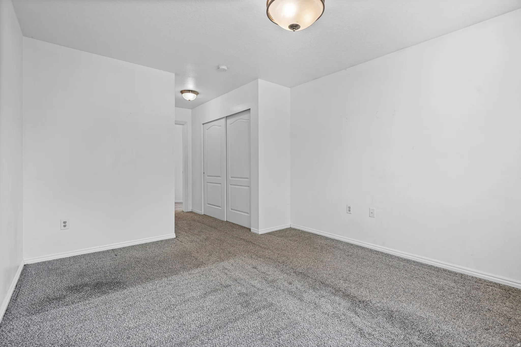 Spacious room featuring gray carpeting, white walls, white trim, and a ceiling-mounted light fixture