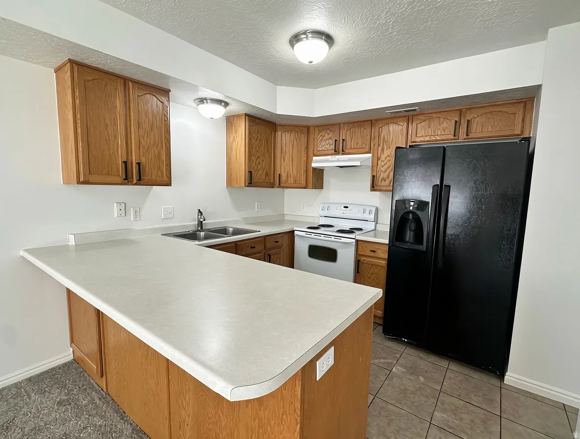 Kitchen featuring wood-finish cabinetry, solid surface countertops, a double basin sink, and a black side-by-side refrigerator