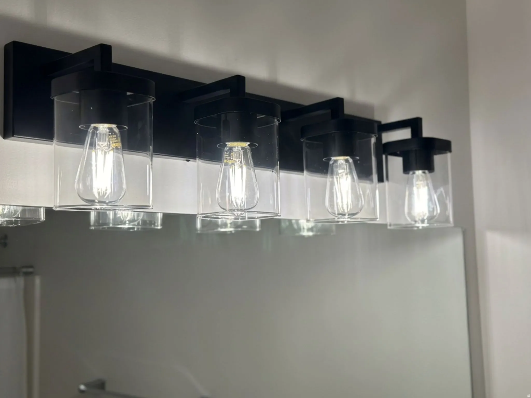 Five-light vanity fixture featuring matte black finish, clear glass shades, and exposed filament bulbs