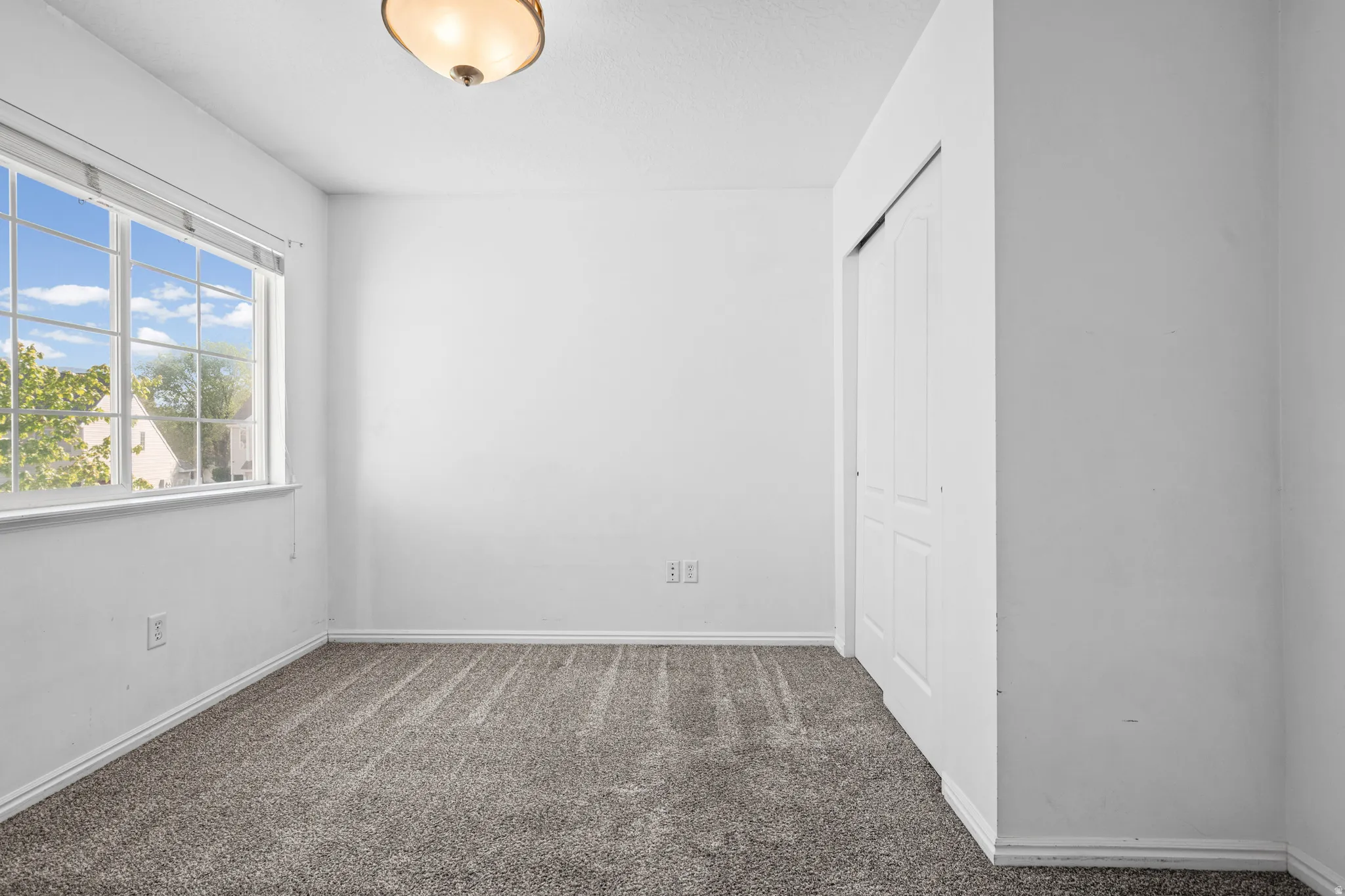 Room featuring neutral wall paint, gray carpet, a multi-pane window, and a built-in closet with sliding doors