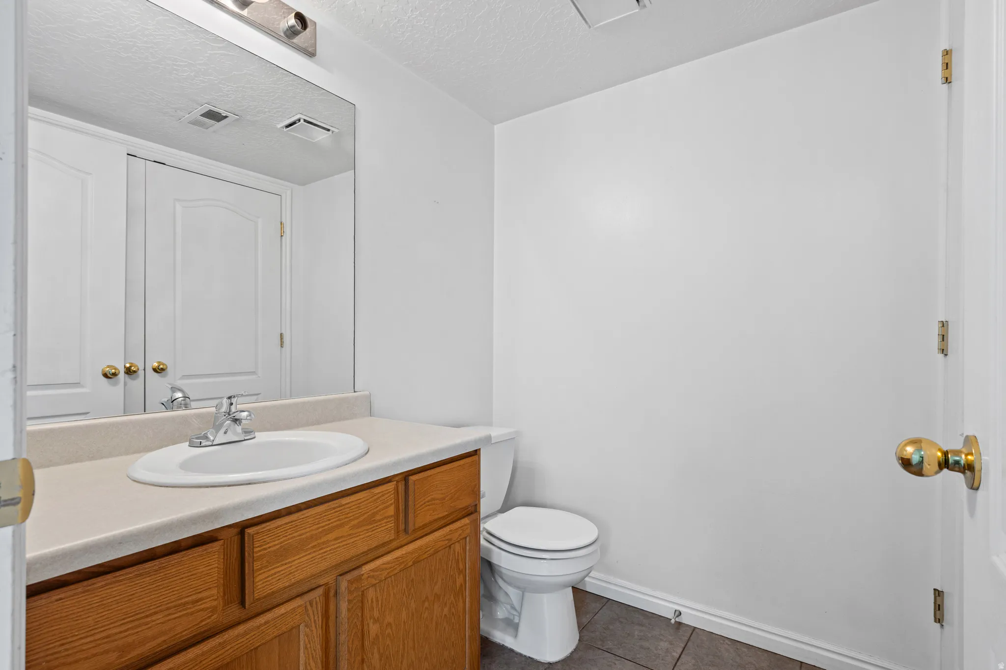 Bathroom featuring a wood-finish vanity with an integrated sink, a light-toned countertop, and an overhead mirror with vanity lighting