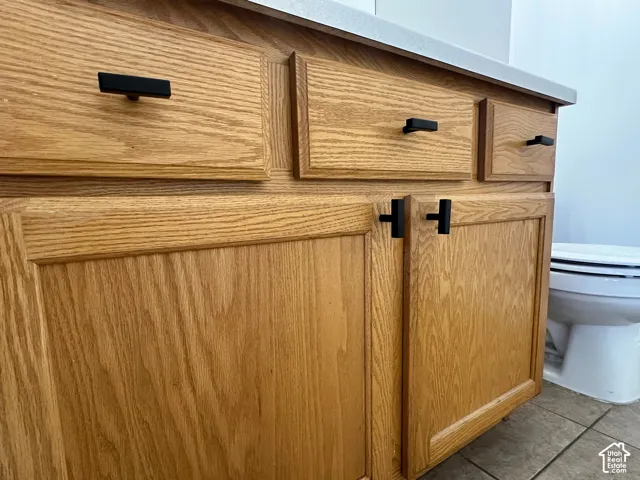 Oak wood-finish cabinetry with black hardware, a light-toned countertop, and tiled flooring