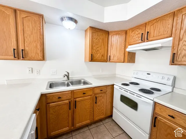 Kitchen featuring wood cabinetry, white countertops, a stainless steel double basin sink, and a white electric range with an overhead exhaust fan
